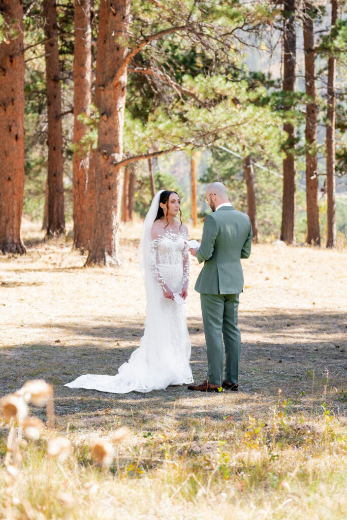 Bride and groom standing together during a private vow ceremony in a Colorado forest surrounded by tall pine trees