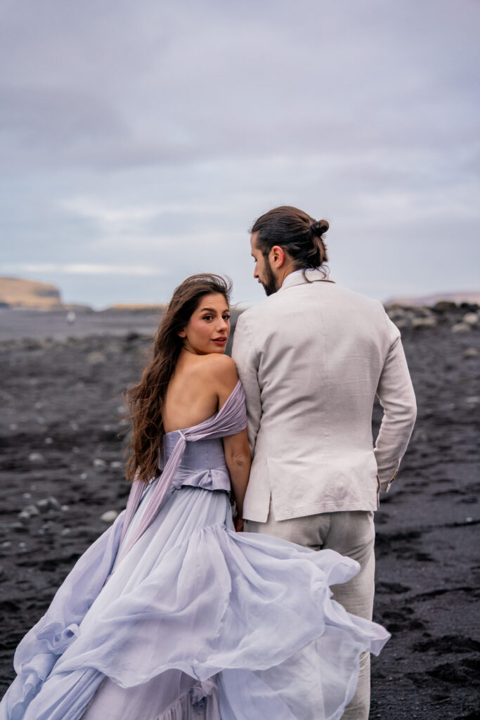 Bride’s flowing dress blowing in the wind during a romantic Iceland black sand beach elopement on the volcanic shoreline.