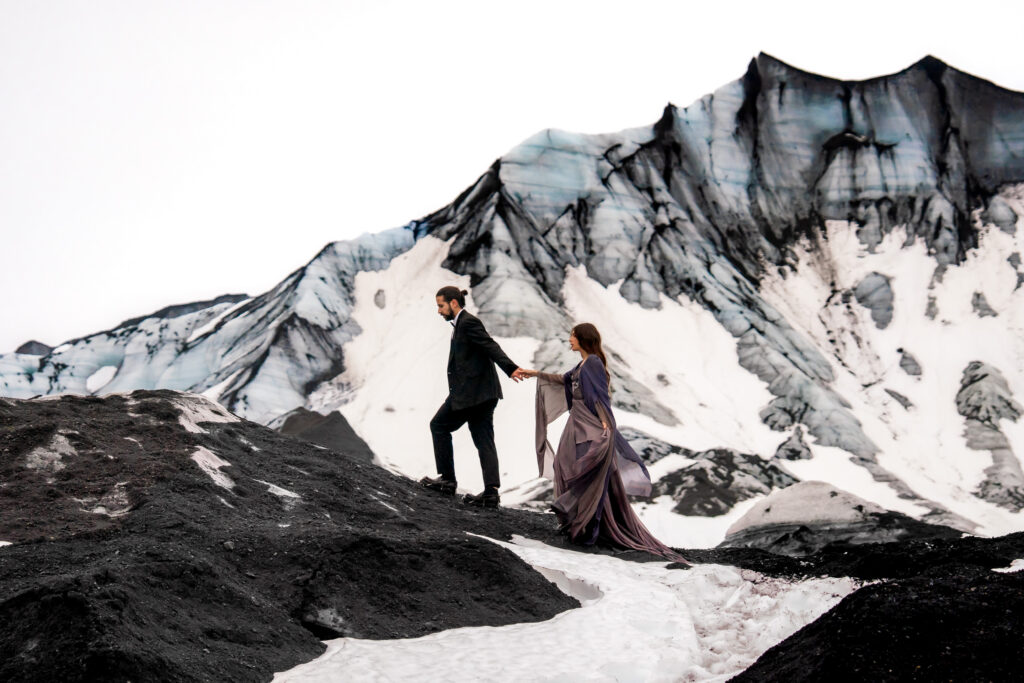 Bride and groom walking together across volcanic terrain near the Katla glacier during their Iceland adventure elopement.