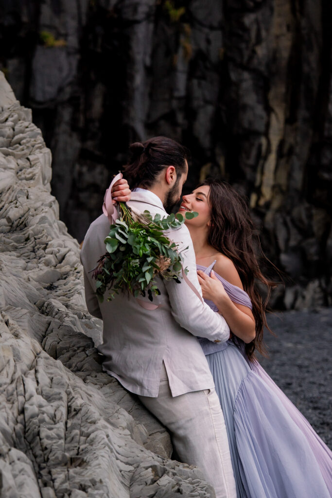 Bride and groom embracing beneath the dramatic basalt cliffs at Reynisfjara during their Iceland black sand beach elopement.