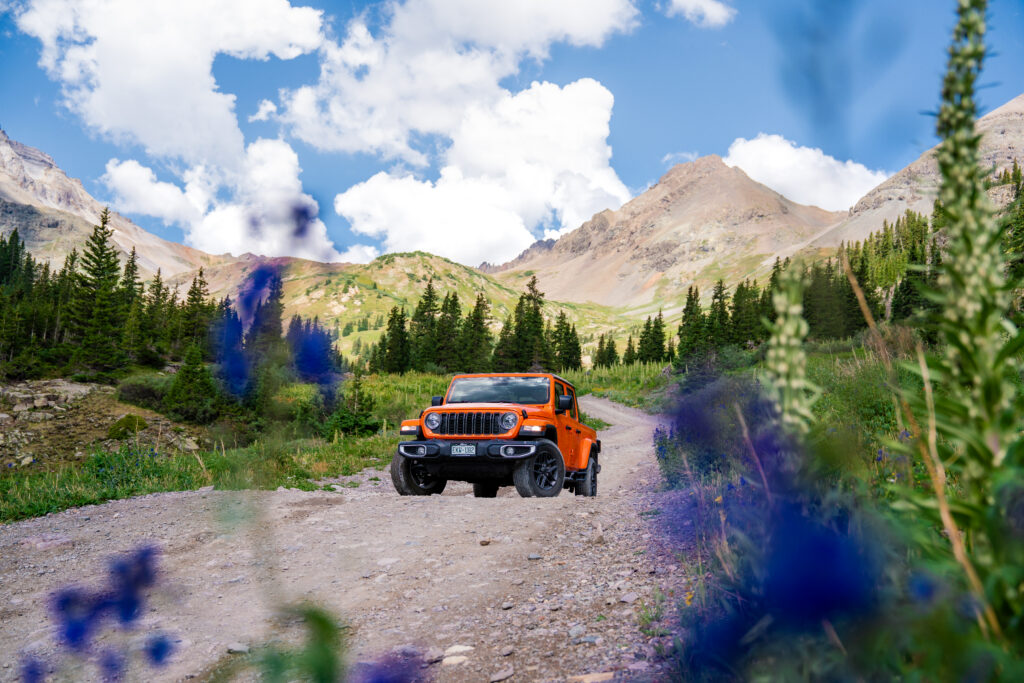 Orange Jeep surrounded by wildflowers while exploring the scenic roads through Yankee Boy Basin near Ouray, Colorado.